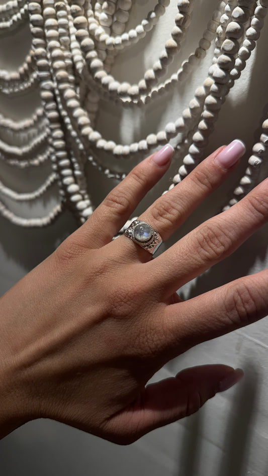 Hand wearing a round rainbow moonstone sterling silver ring with wide ornate boho band.