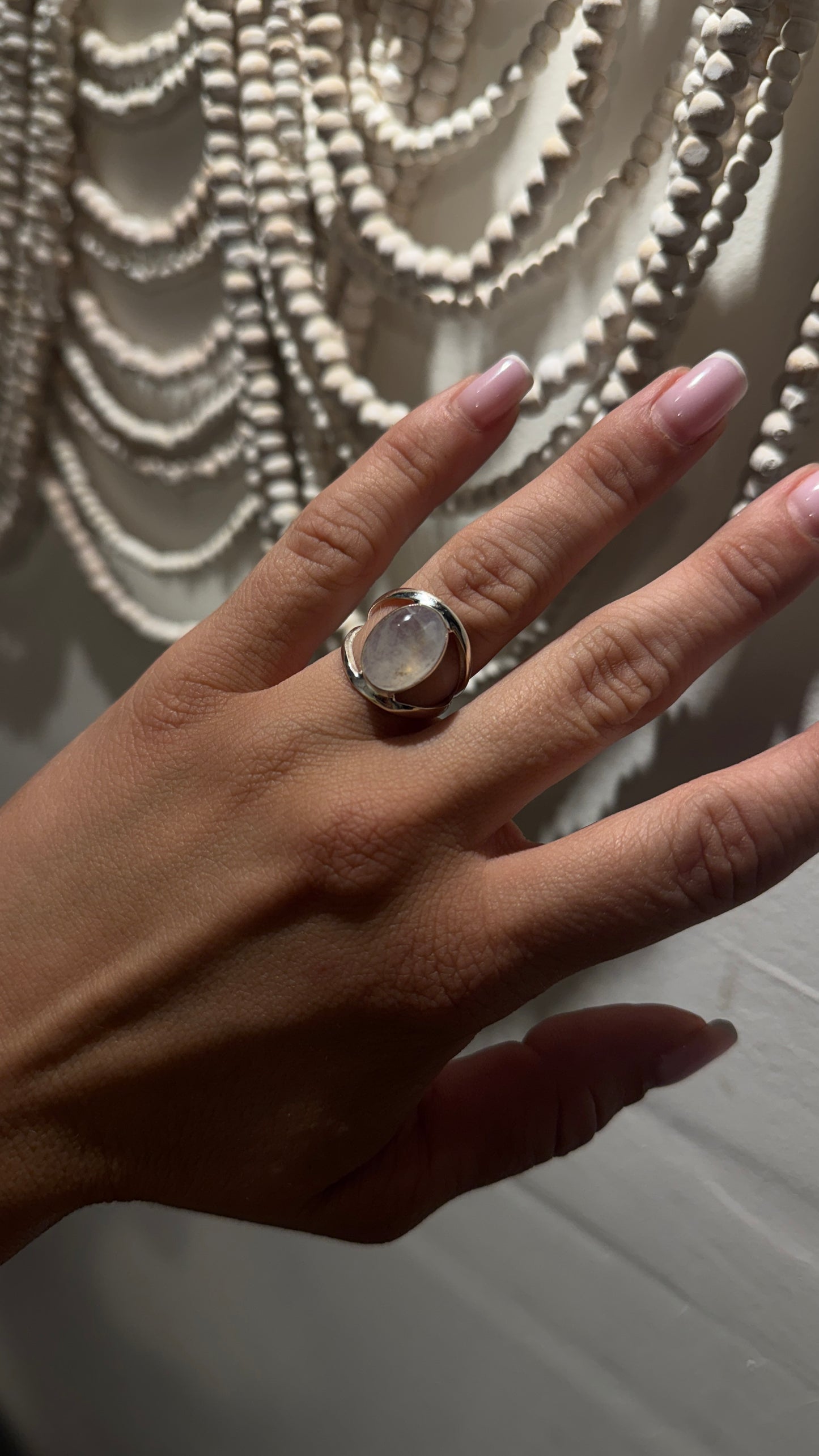 Hand wearing an oval rainbow moonstone ring in sterling silver with a smooth wrap-around setting.
