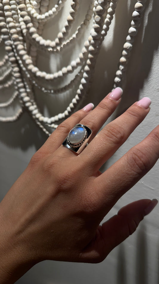Wide sterling silver ring with oval rainbow moonstone and twisted bezel in Eastern-inspired design on hand.