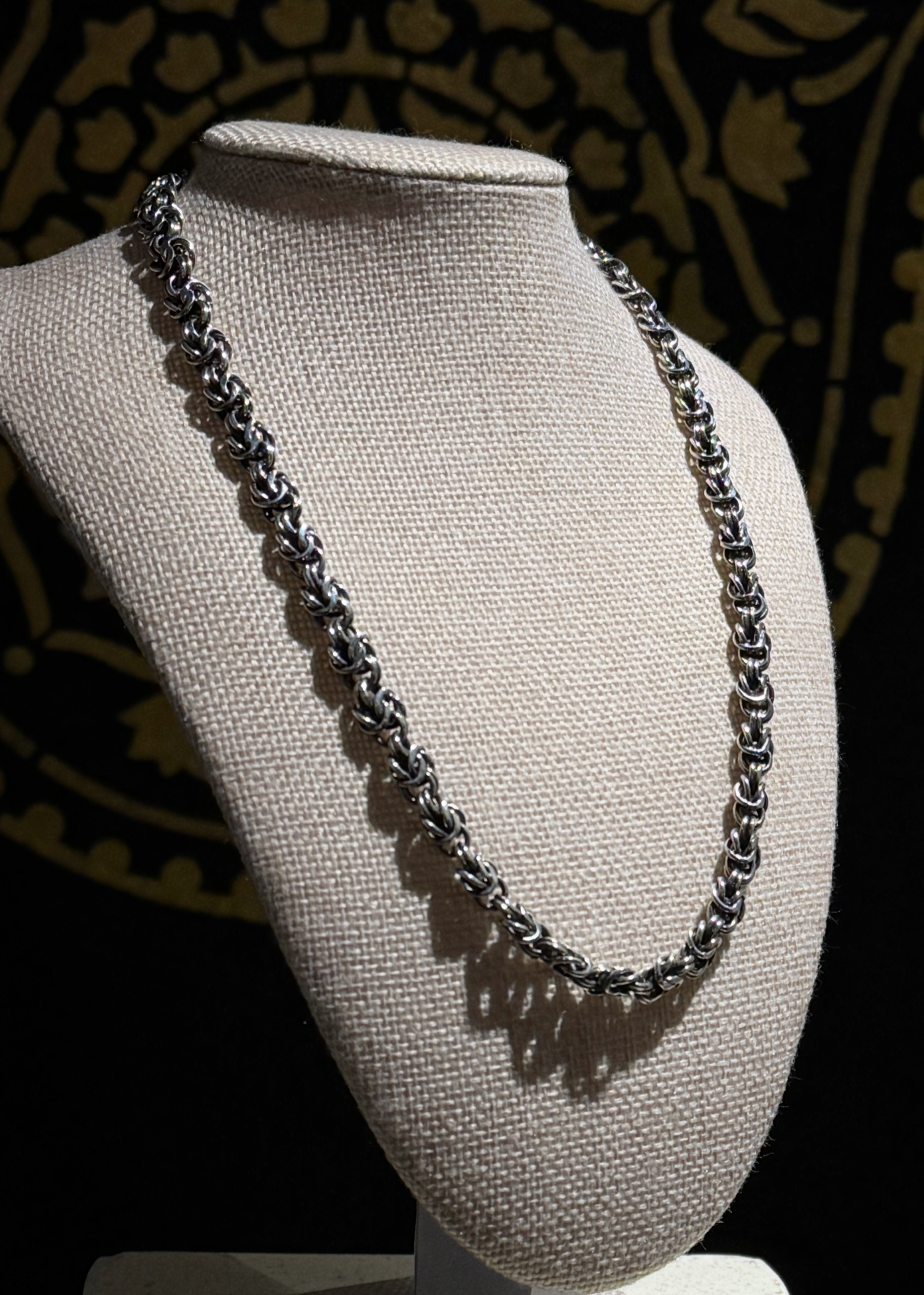 Necklace on a mannequin bust against a dark patterned background