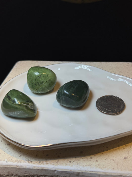 Three green jade tumbled stones on a dish with a quarter for size reference