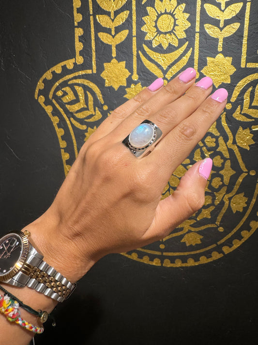 Wide sterling silver ring with oval rainbow moonstone and twisted bezel in Eastern-inspired design on hand.