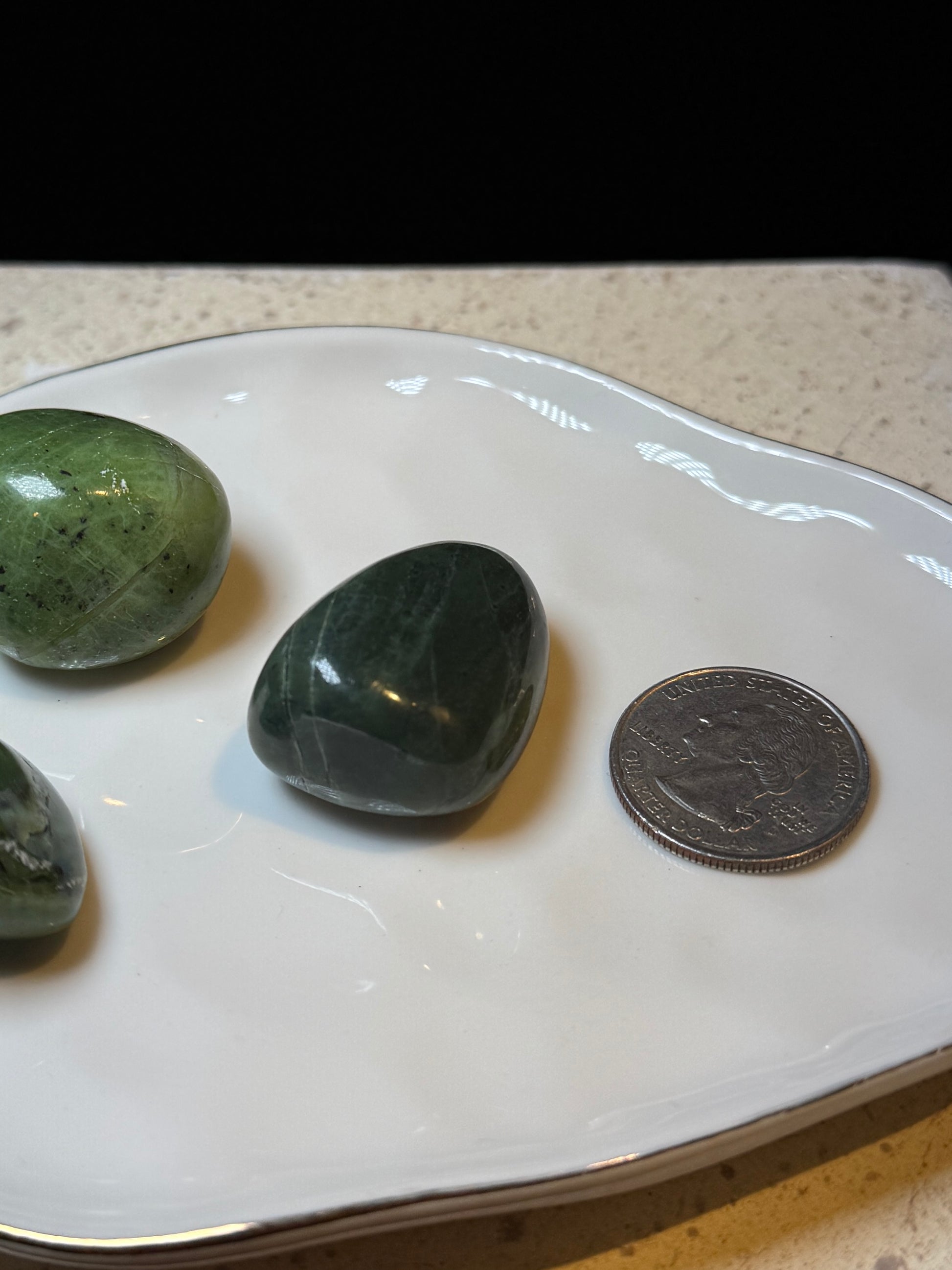 Close-up of polished green jade stone next to a quarter for scale