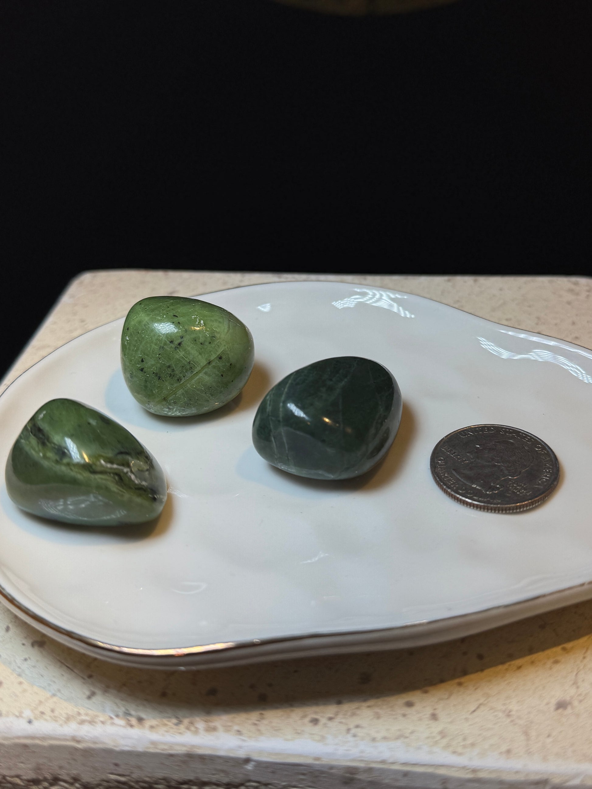 Three green jade tumbled stones on a dish with a quarter for size reference